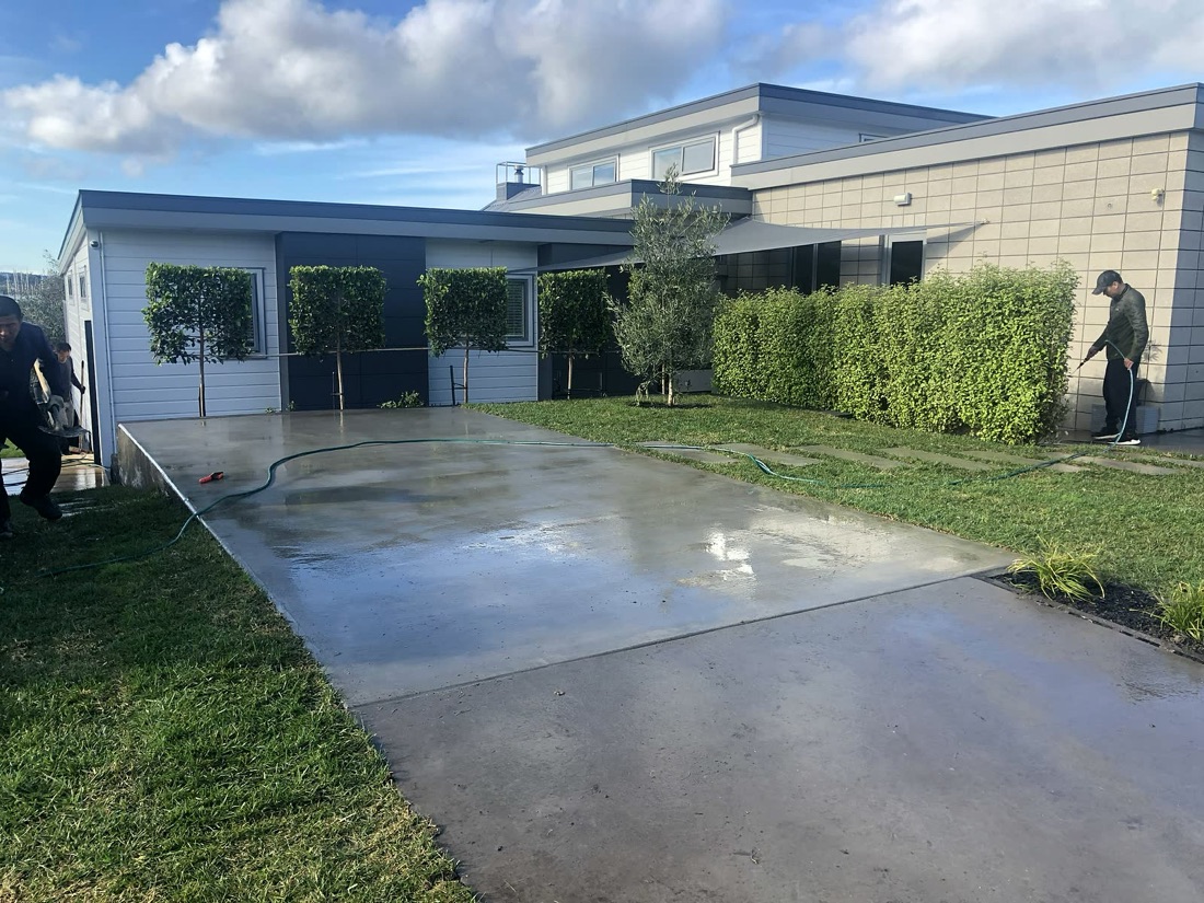 Wet finished concrete driveway beside lawn and hedging